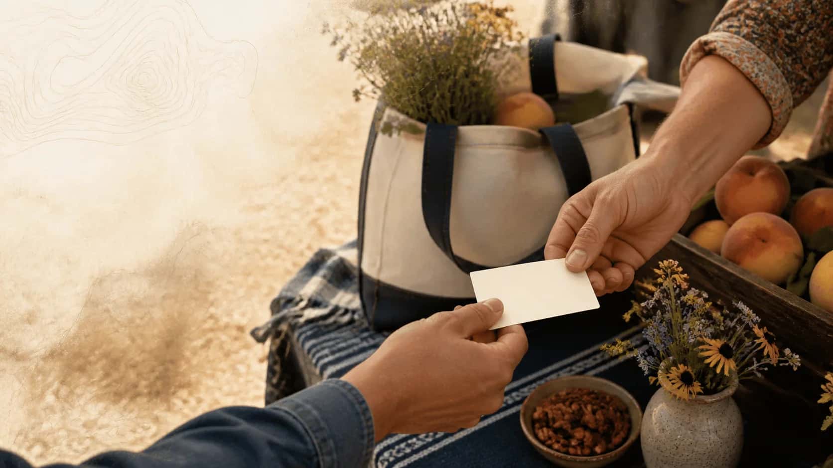 Two people exchanging a blank ivory rectangle across a warm North Texas market table with peaches and prairie flowers